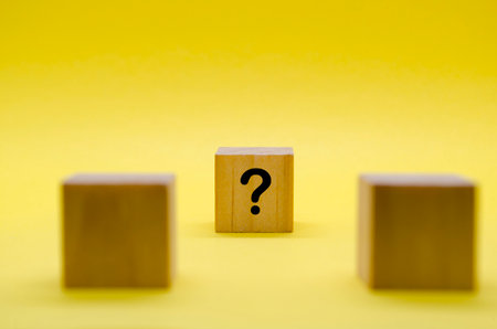 Two wooden cubes with question marks side by side on yellow background.
