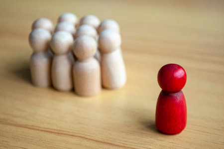 Red Wooden Figure Standing Apart From Beige Peg Group On Table.の写真素材