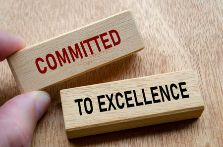 Fingers align wooden blocks that declare commitment to EXCELLENCE, reinforcing an unshakable focus on quality and continuous progress.の写真素材