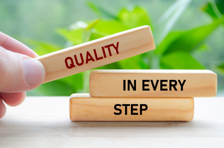 Quality in every step text on wooden blocks held carefully symbolizes continuous improvement and focusの写真素材