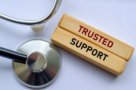 TRUSTED SUPPORT text on wooden blocks beside a stethoscope, Providing trusted medical support and...