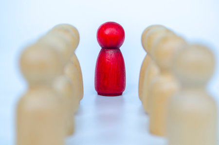 A red figure separated with a visible gap from wooden figures, representing leadership or isolation or discrimination concept.の写真素材