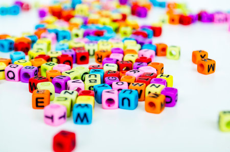 A close up view of vibrant multicolored translucent cubes with alphabet letters scattered across a white surface creating a playful and educational arrangement.の写真素材