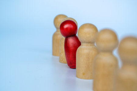 A red wooden figure stands between beige figures, symbolizing courage to speak up in leadership, bullying, or harassment.の素材