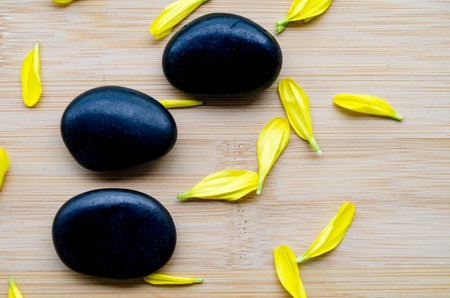 Top view of three zen stones with scattered yellow petals arranged on wood clean look with customizable space for text.の写真素材