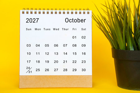 October 2027 neat calendar template with yellow board frame, white sheet design, and small plantの写真素材