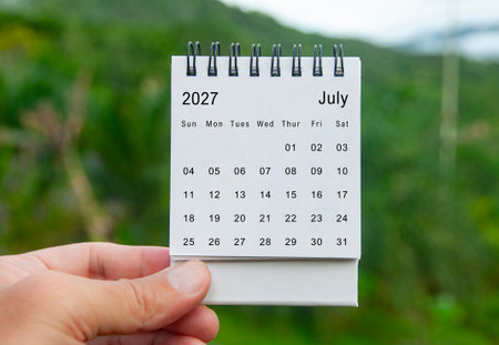 Hand holding July 2027 white calendar with nature background. Holiday and calendar conceptの写真素材