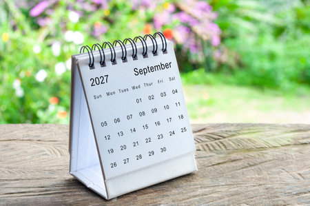 September 2027 spiral desk calendar on rustic wooden table with blurred greenery background