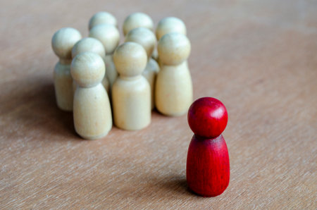 A red figurine confronting a cluster of beige figurines symbolizing opposition that can reflect leadershipの写真素材