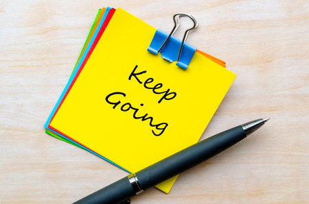 Keep going motivational handwritten text on yellow notepad clipped on wooden deskの写真素材