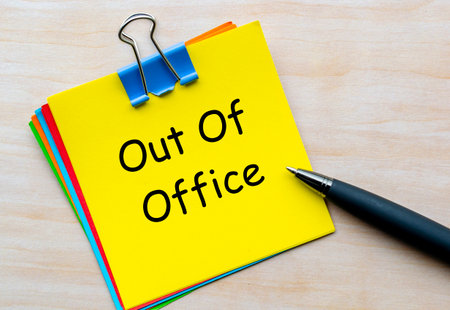Out Of Office, Stack of multicolored notepads with black pen next to them showing announcement of temporary leave from officeの写真素材