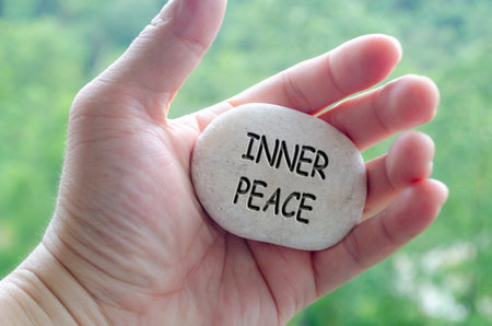 Hand holding a white stone with INNER PEACE text engraved on it, embodying life purpose of serenity and emotional controlの写真素材