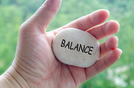 Hand holding a white stone with BALANCE text engraved on it, symbolizing life purpose of harmony and centered livingの写真素材