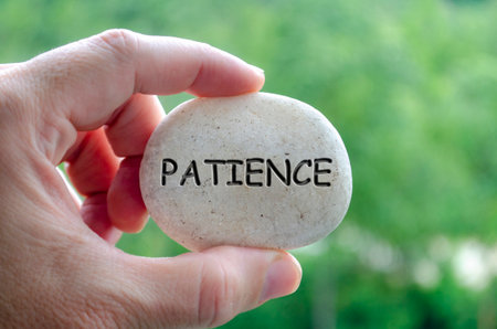 Hand holding a white stone with PATIENCE text engraved on it, symbolizing life purpose of calm endurance and trust in timing.の写真素材