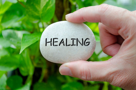 Hand holding a white stone with HEALING text engraved on it, symbolizing life purpose of recovery and restorationの写真素材
