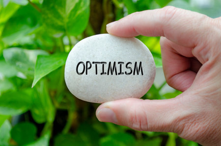 Hand holding a white stone with OPTIMISM text engraved on it, reflecting life purpose of hope and positive outlookの写真素材