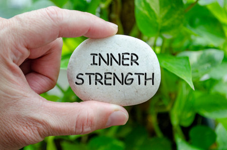Hand holding a white stone with INNER STRENGTH text engraved on it, representing life purpose of...