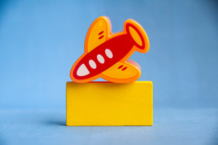 Red and yellow toy airplane on yellow block with blue background symbolizing travel, creativity, and imagination with customizable space for text or ideas.の写真素材
