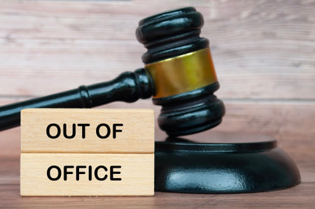 Out of office text on wooden blocks with gavel background.