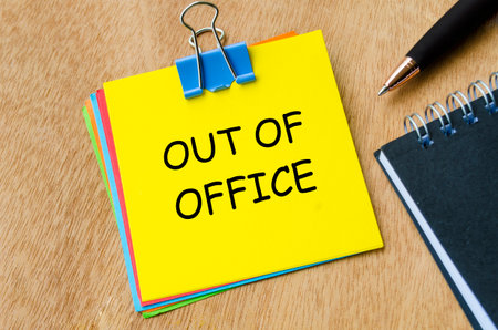 Out of office text on yellow notepad with pen and an notebook background. Getaway or on a vacation conceptの写真素材