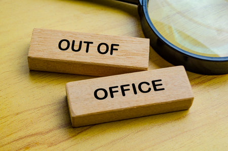 Out of office text on wooden blocks with magnifying glass background. Getaway or on a vacation conceptの写真素材