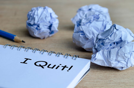 A dramatic workspace scene with crumpled paper surrounding a notepad that displays the handwritten message I Quit, symbolizing stress and burnoutの写真素材