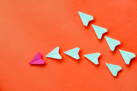 Colorful paper airplanes flying together on orange background expressing innovation diversity and...
