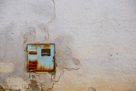 An old and rusty electricity meter fits perfectly in a very deteriorated wall of one street of the colonial town of Villa de Leyva, in the Andean mountains of central Colombia.の写真素材