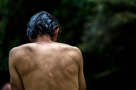 Detail of the wet back of a swimmer sitting on a rock at the bank of a river in the temperate land...