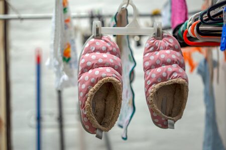 A pair of pink slippers hanging from a cloth hanger in a indoor clothesline.