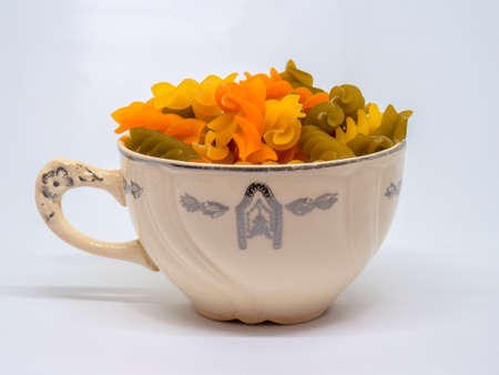 Studio shot of a heap of colorful raw fusilli pasta on a vintage porcelain cup against neutral...