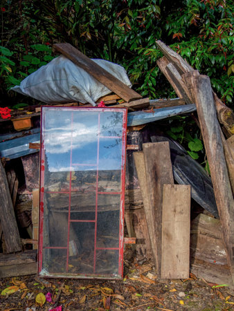 A discarded old red framed window placed among different objects, reflects the afternoon sky in a farm near the town of Arcabuco in central Colombia.の写真素材