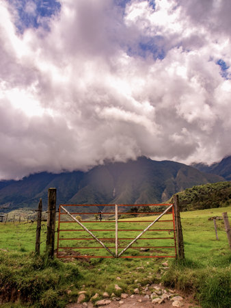 The old and rusted metal red and white gate of a cattle farm , captured in an overcast day at the edge of a rural road near the town of La Palma in the central Andes of Colombia.の写真素材