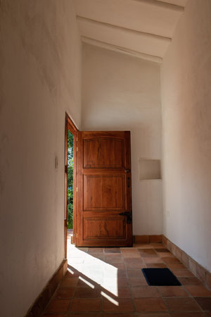 Hallway with an wooden open door and a small rug, illuminated by the morning sun, in a farmhouse at...