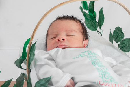 Beautiful newborn baby (4 days old), sleeping in bamboo fiber basket and surrounded by green leaves. close-up top view, healthy doctor conceptの写真素材