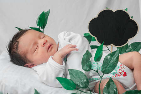 Beautiful newborn baby (4 days old), sleeping in bamboo fiber basket and surrounded by green leaves. with space for advertising text in black cloud shape,の写真素材