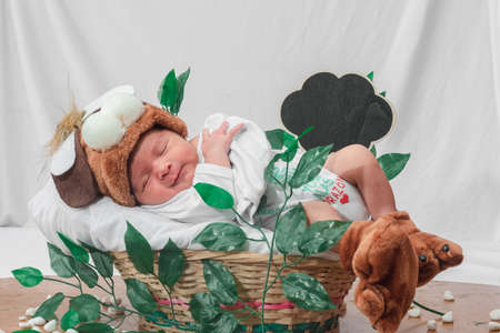 Beautiful newborn baby (4 days old), with hat and puppy shoes, in bamboo fiber basket and surrounded by green leaves, Healthy medical conceptの写真素材