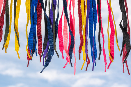 many colored shoelaces, hanging on a background of sky and clouds, pointed downの写真素材