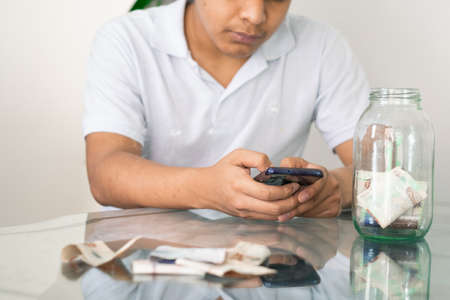 man doing online shopping, bad financial situation, guy texting on his mobile phone, banknotes on the table, bankrupt young man, spending his savings. economic conceptの写真素材