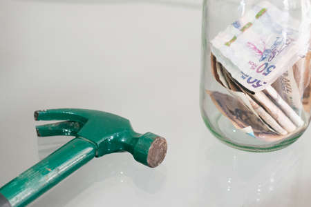 hammer next to glass jar full of banknotes. hammer to break glass piggy bank. concept of economy and personal savingsの写真素材