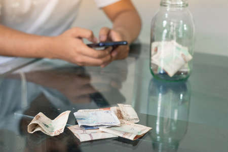 man doing online shopping, bad financial situation, guy texting on his mobile phone, banknotes on the table, bankrupt young man, spending his savings. economic conceptの写真素材