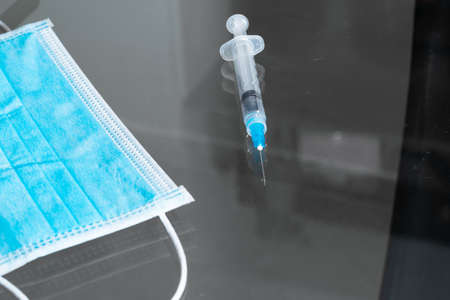 top view of syringe and blue hygienic protective mask, on the glass table, ready to be used for vaccination. instruments for vaccination (covid-19, influenza) pandemic and health conceptの写真素材