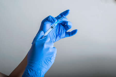 the doctor's hands with blue rubber gloves, holding and tapping a syringe ready for vaccination. vaccination and protection tools (covid-19, influenza) pandemic and health conceptの写真素材