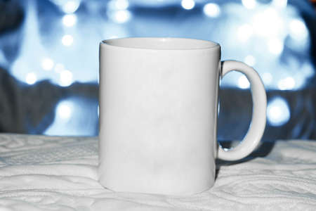 white mug on the bed, mug on white cloth, space for advertising text, blue background. defocused lights background. advertising concept. sublimationの写真素材