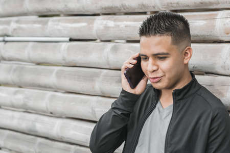 young latino, university student talking on his cell phone with happiness on his face, leaning on a guadua hut, young entrepreneur and influencer with his cell phone in his hand. technological conceptの写真素材