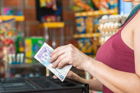 latina woman's hand opening the cash register. taking out money after making a sale, girl working in colombian neighborhood store. fifty thousand pesos bill. concept of entrepreneurship.の写真素材