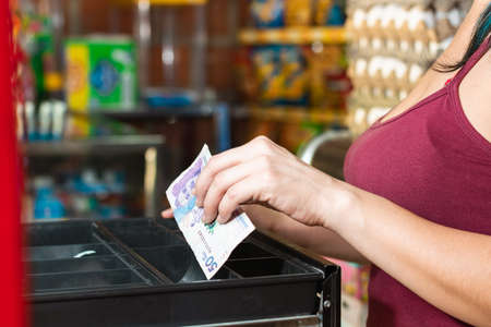 latina woman hand in red blouse opening cash register. taking out money after making a sale, girl working in colombian neighborhood store. entrepreneurship concept.の写真素材