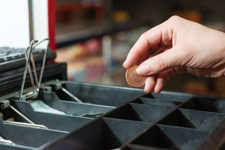 close-up detail of latin woman's hand taking money from the cash register, making a sale in her...