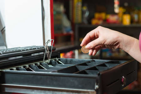 latina woman's hand taking money from the cash register, making a sale in her grocery store, girl taking with her hand a Colombian thousand peso coin. concept of economy and businessの写真素材