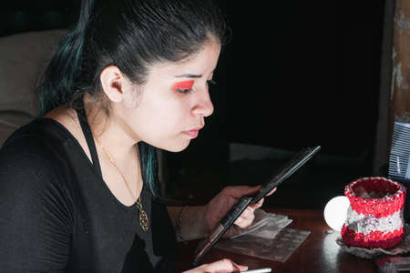 beautiful latina woman with green hair, in front of her dressing table making up her eyes with a red eye shadow. girl observes if she is well made up. black background. beauty concept.の写真素材